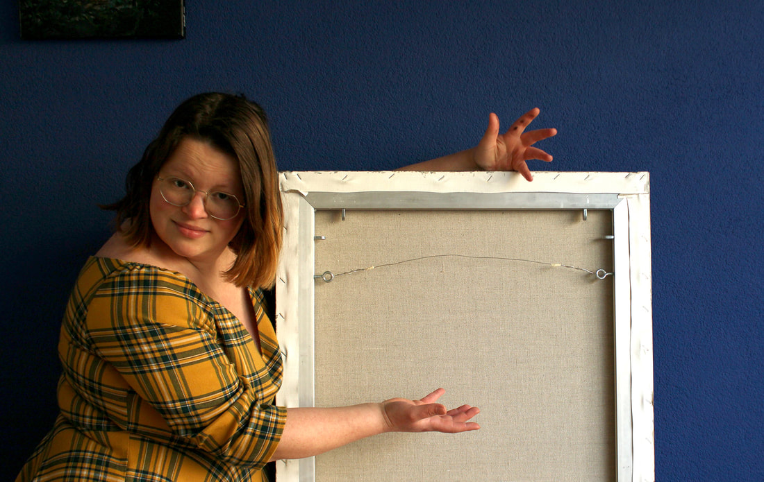 Foto Renée in gele jurk, wijst naar achterkant van schilderij.